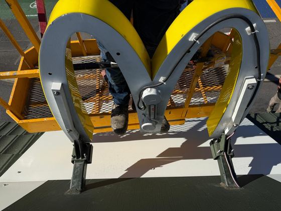 Pose d'un logo en forme d'arche depuis une nacelle : fixations et câblage en cours.