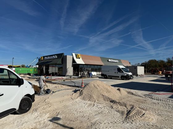 Bâtiment en fin de chantier avec son enseigne et son auvent, engins et matériaux au sol.